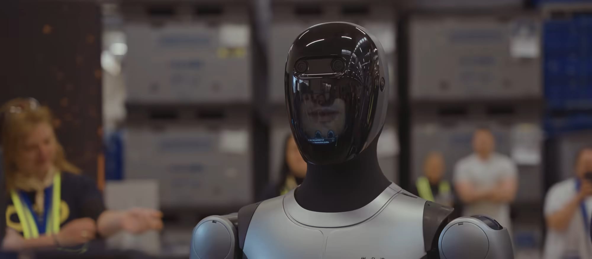 Humanoidni robot MAX hodi med delavci po proizvodni hali.